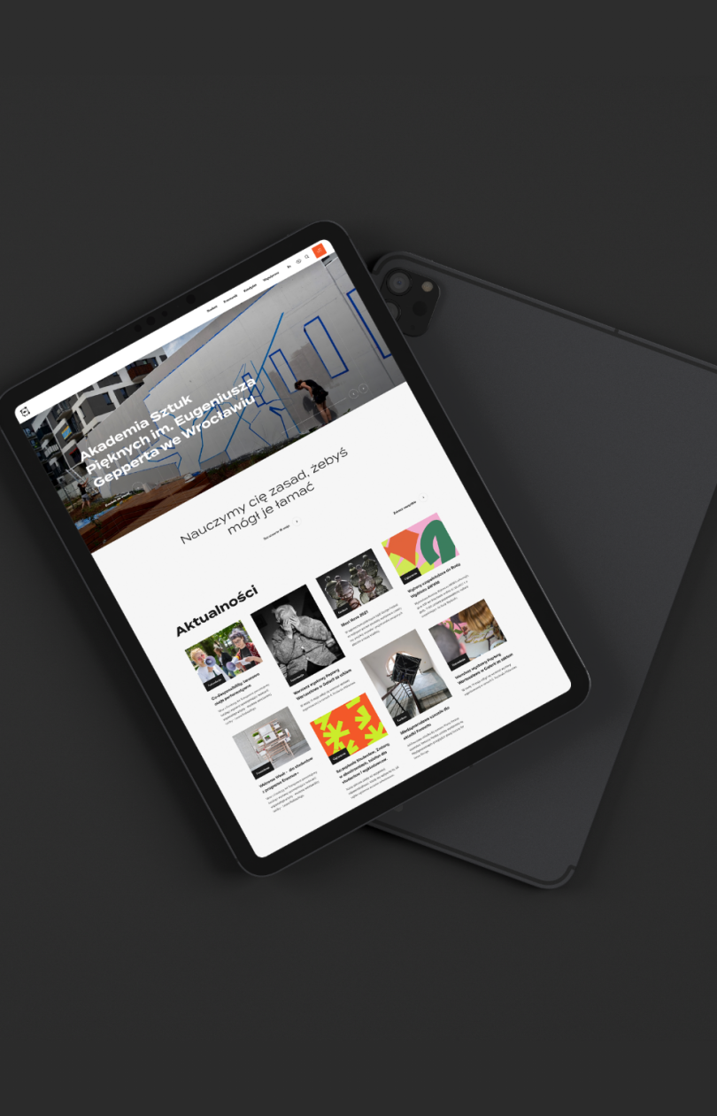 Tablet wyświetlający stronę internetową Akademii Sztuk Pięknych im. Eugeniusza Gepperta we Wrocławiu, z widocznym nagłówkiem, hasłem „Nauczymy cię zasad, żebyś mógł je łamać” oraz sekcją aktualności zawierającą miniatury artykułów i wydarzeń.